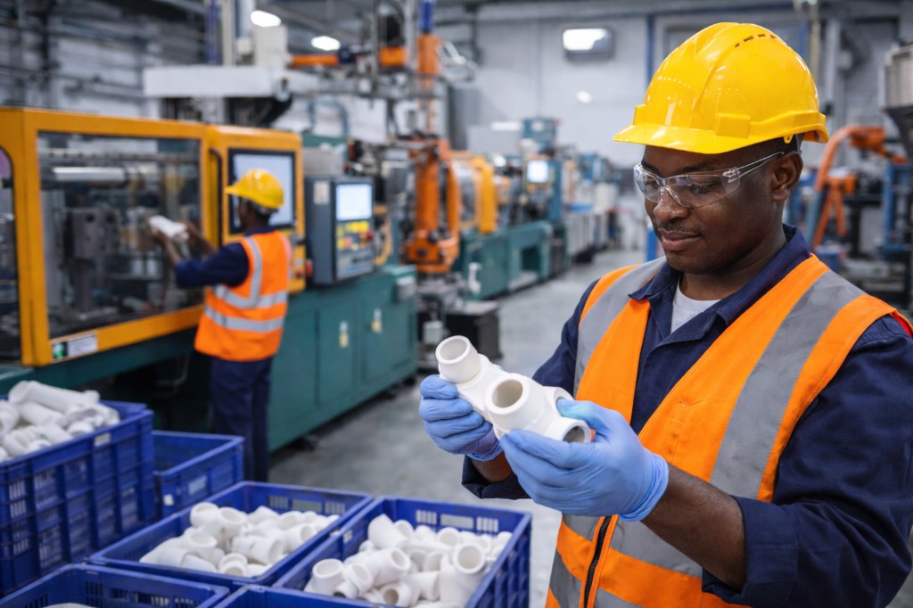 Plastics manufacturing: worker inspecting plastic pipe fitting, injection molding and production